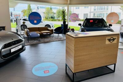 MINI Verkaufsraum Freilassing - im Hintergrund eine Sitzecke, im Vordergrund ein Empfangscounter, rechts im Bild ein silberner MINI